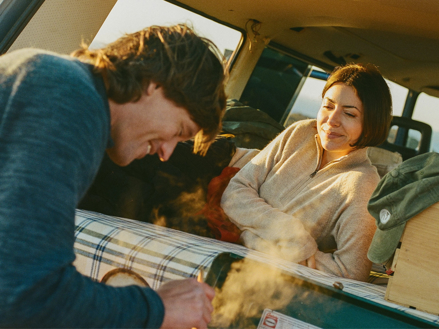 Woman wearing a beige alpaca quarter-zip sweater, relaxed fit, smiling inside a camper van at sunset