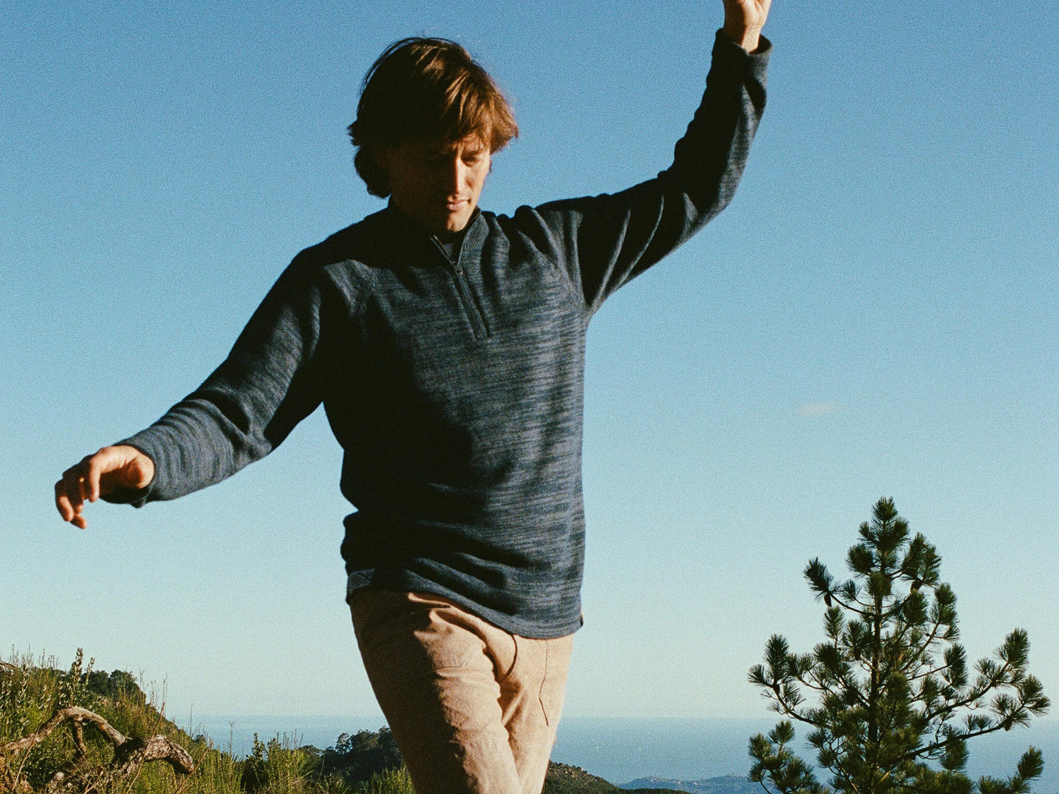 Man wearing a navy heather alpaca quarter-zip sweater in a relaxed fit balancing on a sunny hillside