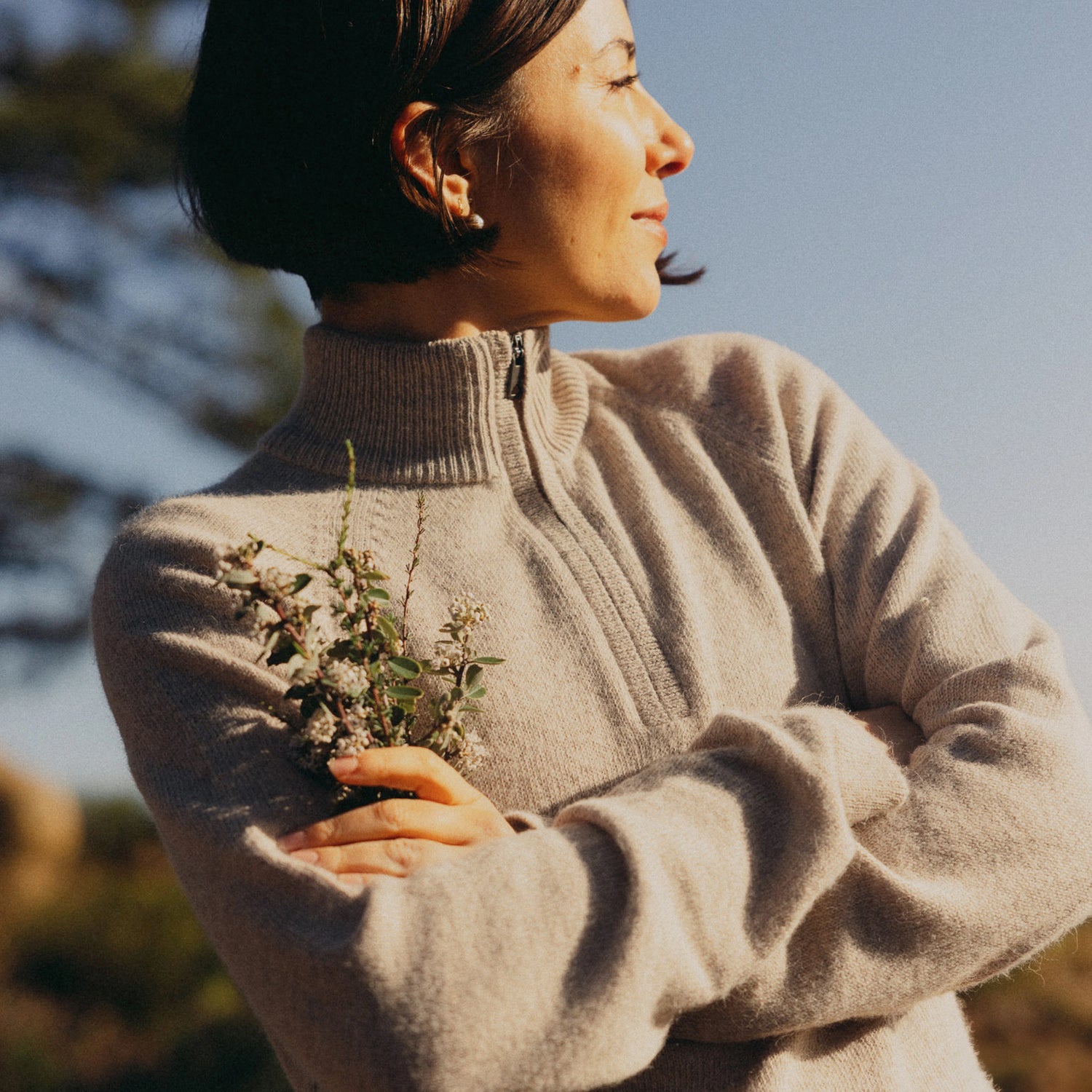 Woman wearing a tan alpaca quarter-zip sweater with relaxed fit, facing right outdoors against clear sky