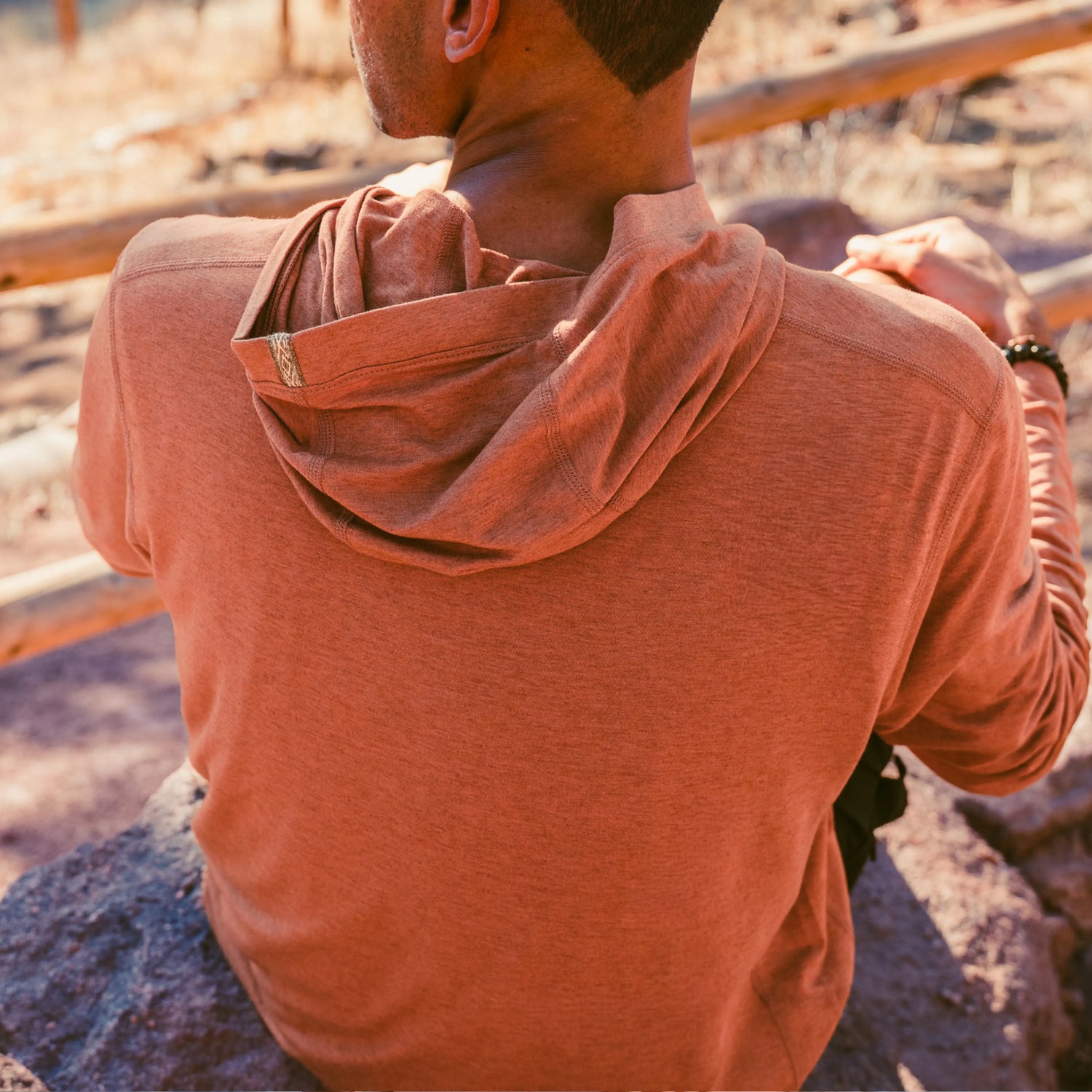 Rear view of Men’s Sol Crew long sleeve UPF sun shirt in rust, relaxed fit on model with draped hood at sunny outdoor trail