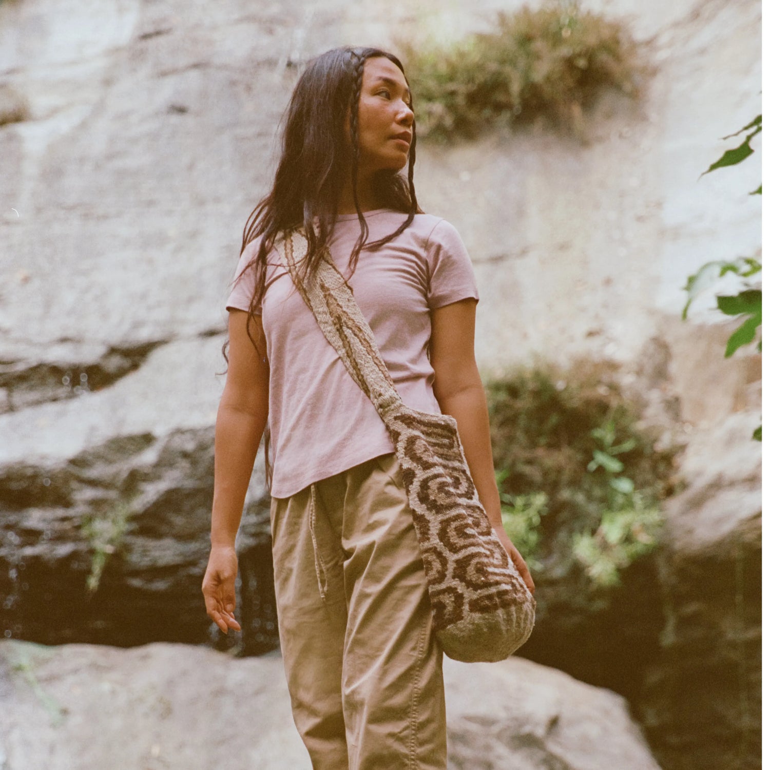 Woman wearing light pink Women’s Essential Tee standing on a rocky trail near a waterfall, casual outdoor setting