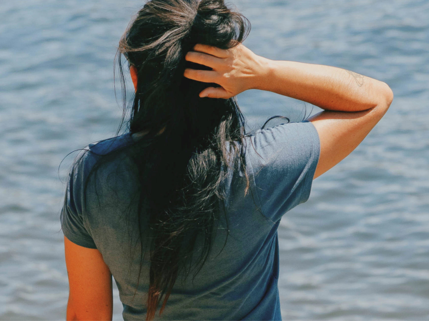 Rear view of Women’s Essential Tee in navy showing short sleeves and relaxed fit on model by the water