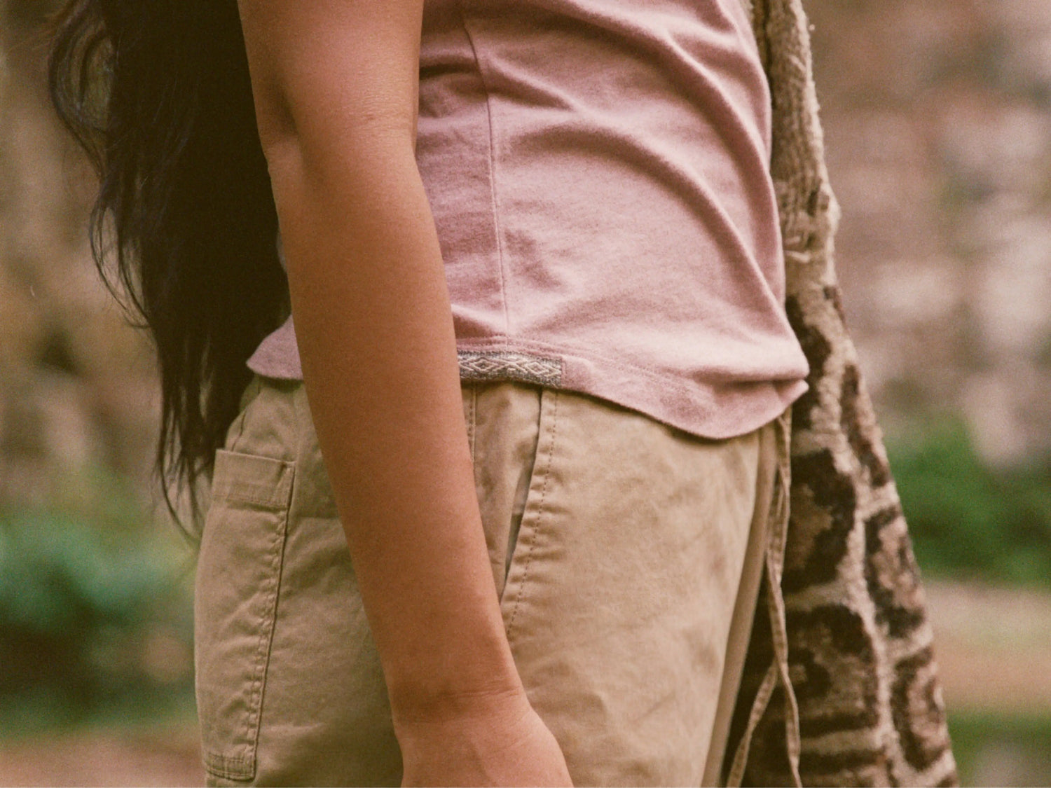 Woman cropped side view wearing the women’s essential V-neck in Woodrose and tan shorts, showing the shirt’s fit at the waist outdoors