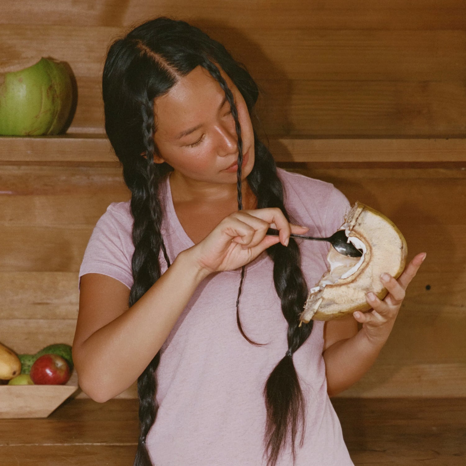 Woman wearing light pink Women’s Essential V-neck tee, relaxed-fit, scooping coconut with spoon against wooden backdrop