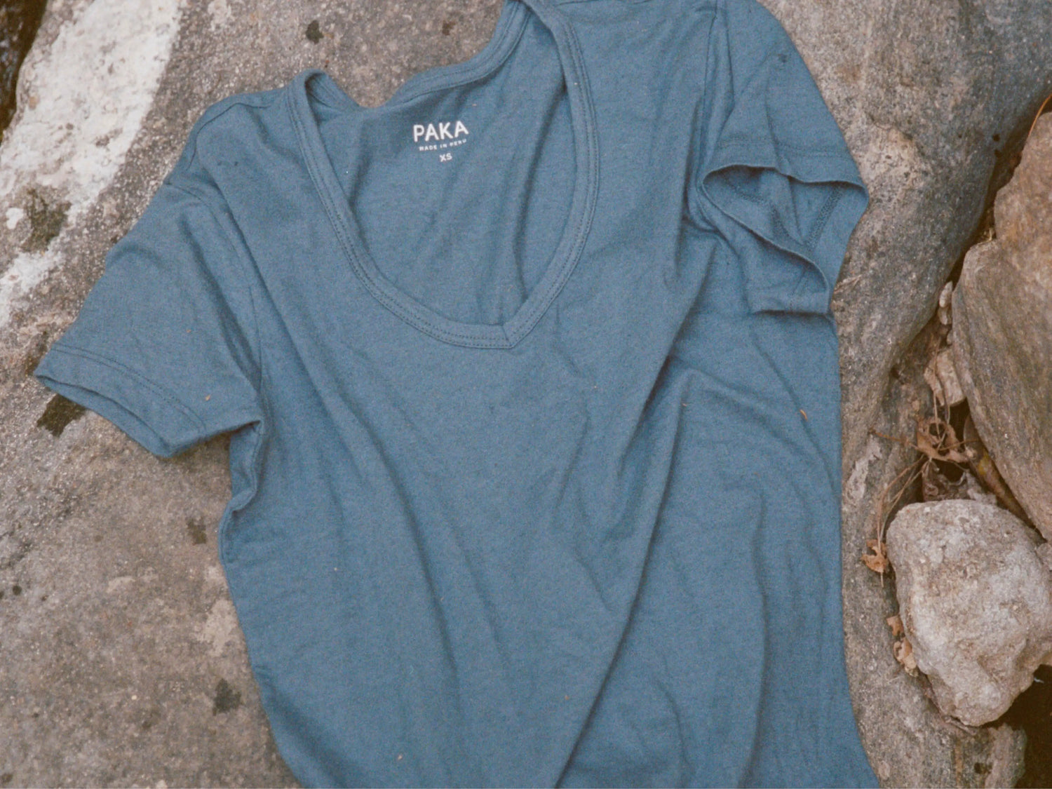 Flat lay of Women’s Essential V-neck t-shirt in bluestone showing V-neck and short sleeves on a rocky background