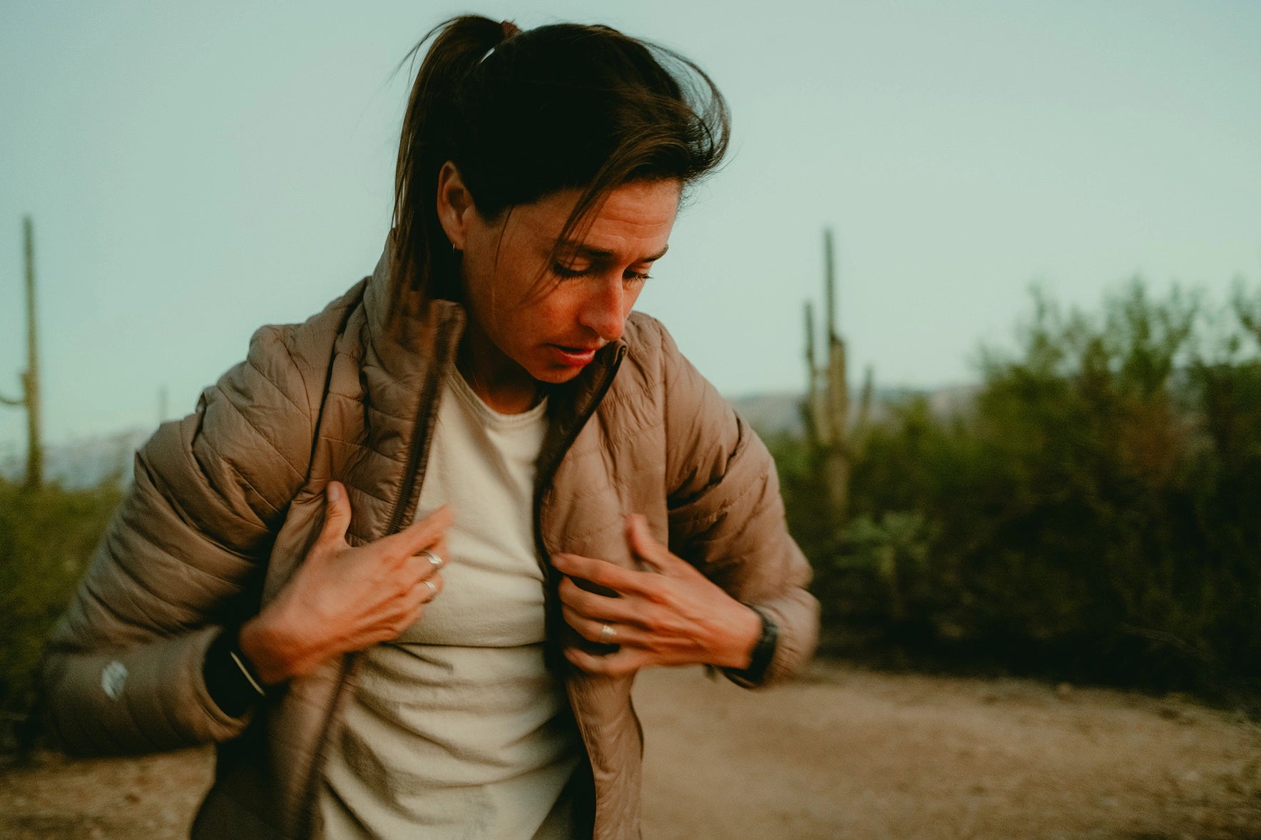 Person adjusting collar while wearing a tan Mayu Ultralight jacket outdoors on a grassy trail