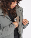 Three-quarter view of Apu Parka on a woman showcasing interior zip chest pocket holding a smartphone on white background