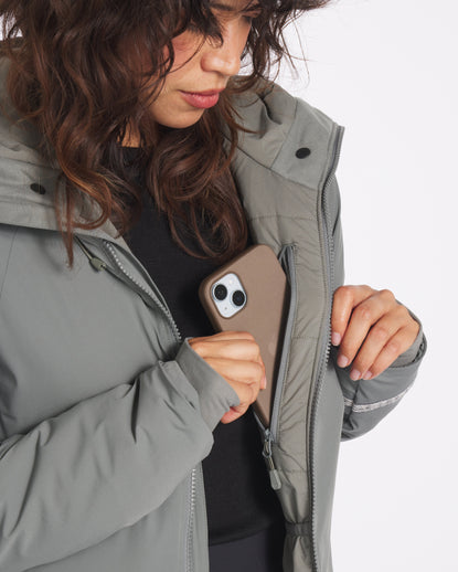 Three-quarter view of Apu Parka on a woman showcasing interior zip chest pocket holding a smartphone on white background