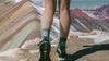 Hiker standing on layered, colorful rock formation wearing green mid-calf trail crew socks and hiking shoes