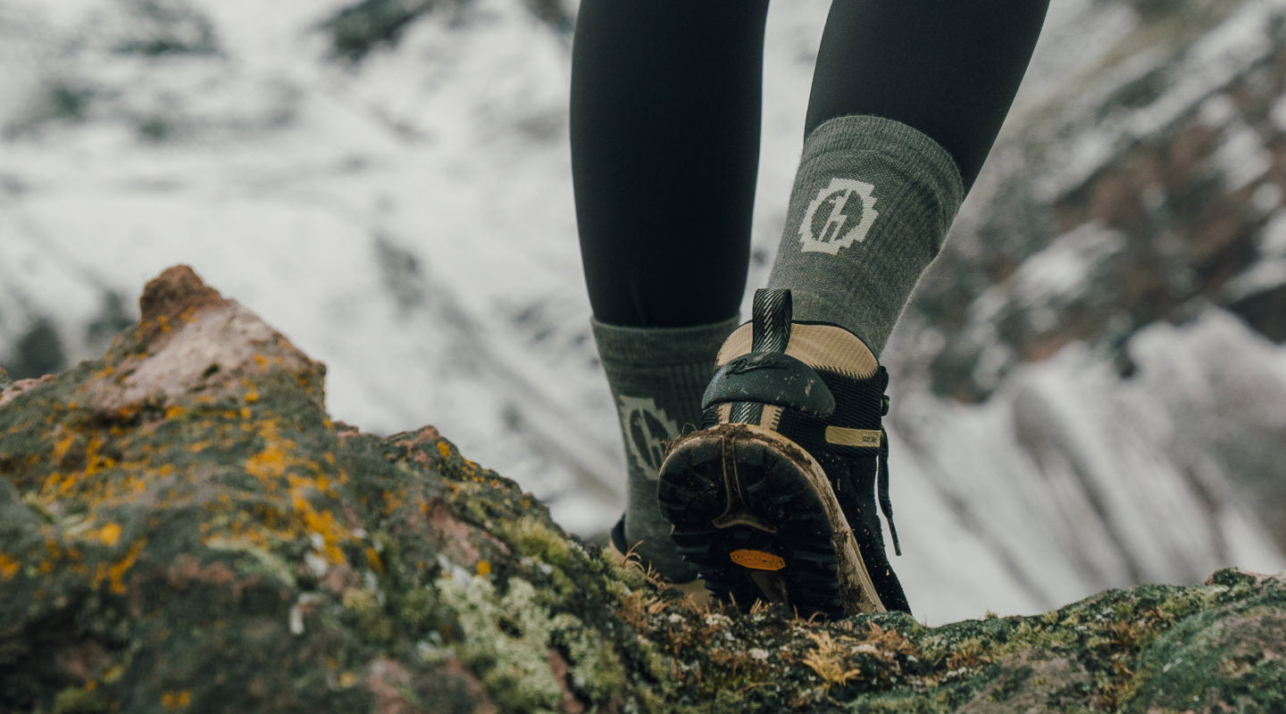 Hiker wearing black PAKA trail crew socks on a rocky trail, showing ribbed calf and heel padding