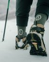Hiker wearing crew-length socks and trail shoes walking through snow with a trekking pole