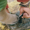 Hiker tightening shoe while wearing a tan Paka performance crew trail sock on a rocky trail