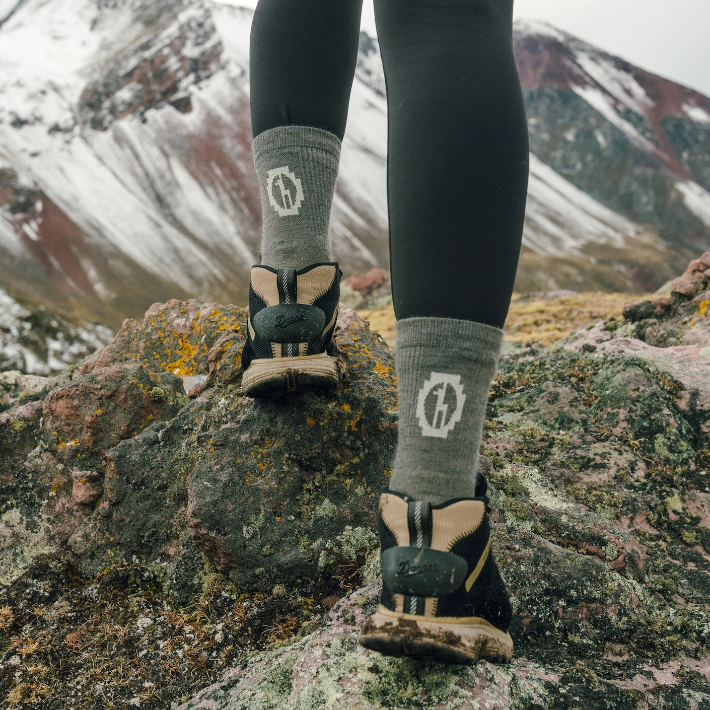 Rear view of Trail 3/4 Crew socks in gray showcasing cuff logo and mid-calf height with rocky, snow‑topped mountain background
