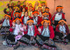Quechua women weavers smiling and waving outside Pisac wearing traditional red jackets, embroidered skirts, and orange headpieces