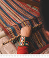 Close up of hands weaving a colorful striped textile on a loom, showing traditional pattern and a bracelet on the wrist
