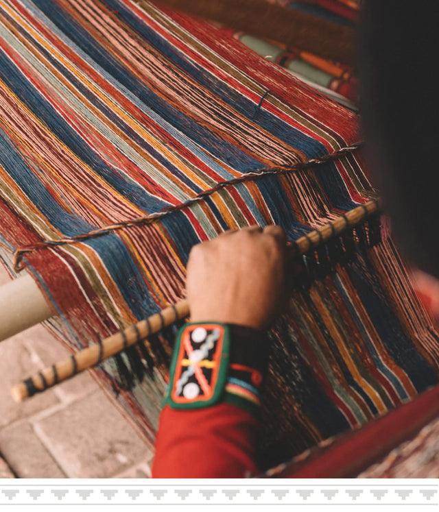 Close up of hands weaving a colorful striped textile on a loom, showing traditional pattern and a bracelet on the wrist