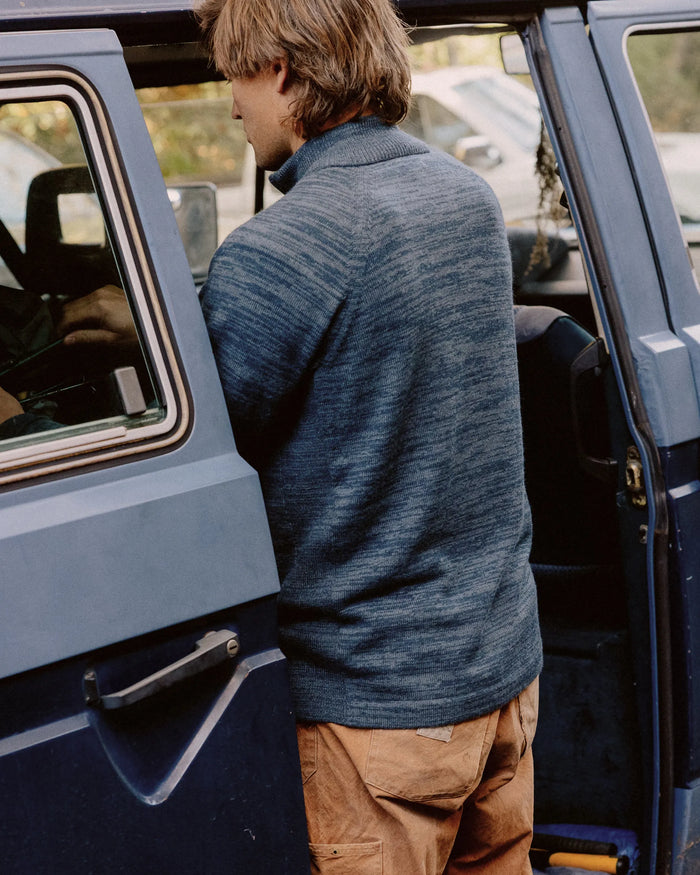 Man wearing navy alpaca wool quarter zip sweater standing at an open car door, back view showing relaxed fit and ribbed collar