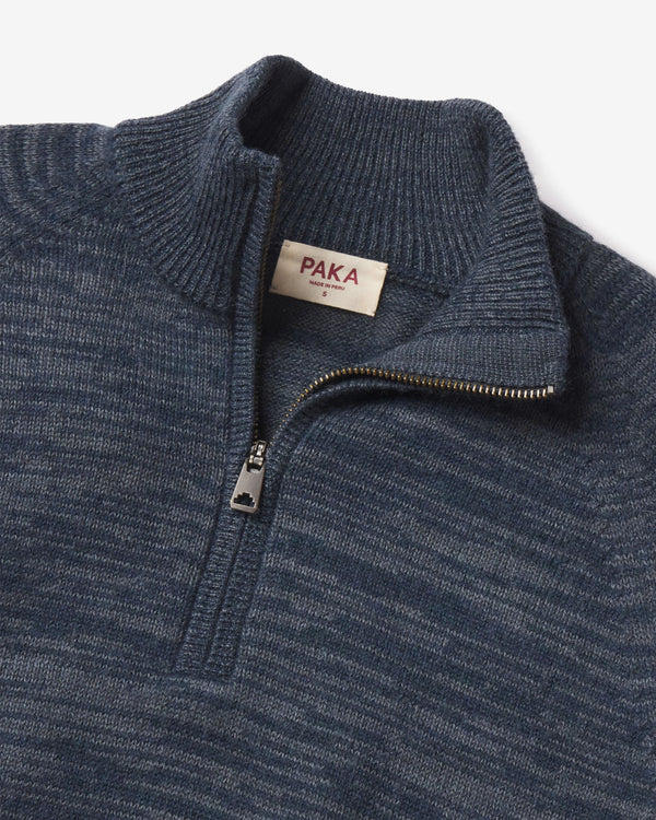 Top-down close-up of The Quarter Zip alpaca sweater with ribbed stand collar, metal zipper and PAKA label on gray background