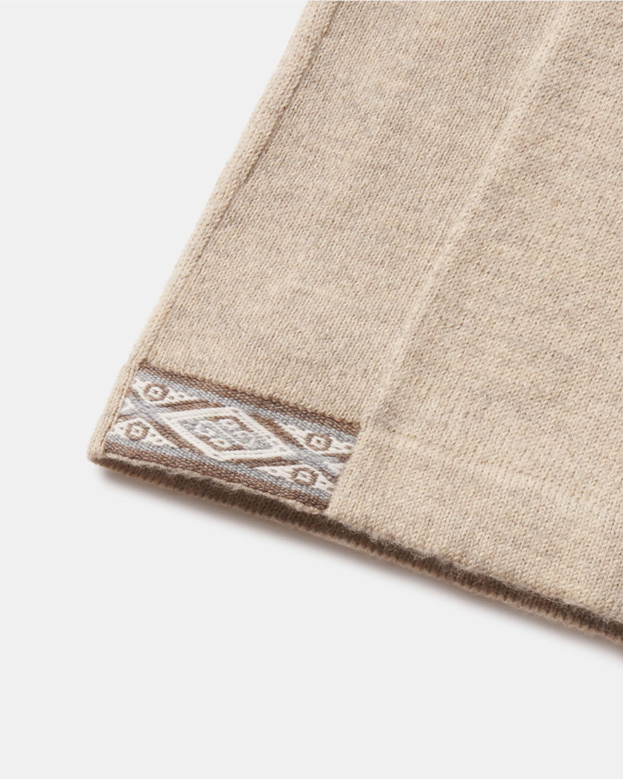 Close-up of The Quarter Zip hem showing beige alpaca knit and decorative patterned trim on a white background