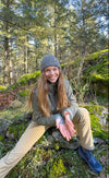 Rachael Tancock sitting on mossy rocks in a forest, wearing a PAKA alpaca parka and beanie