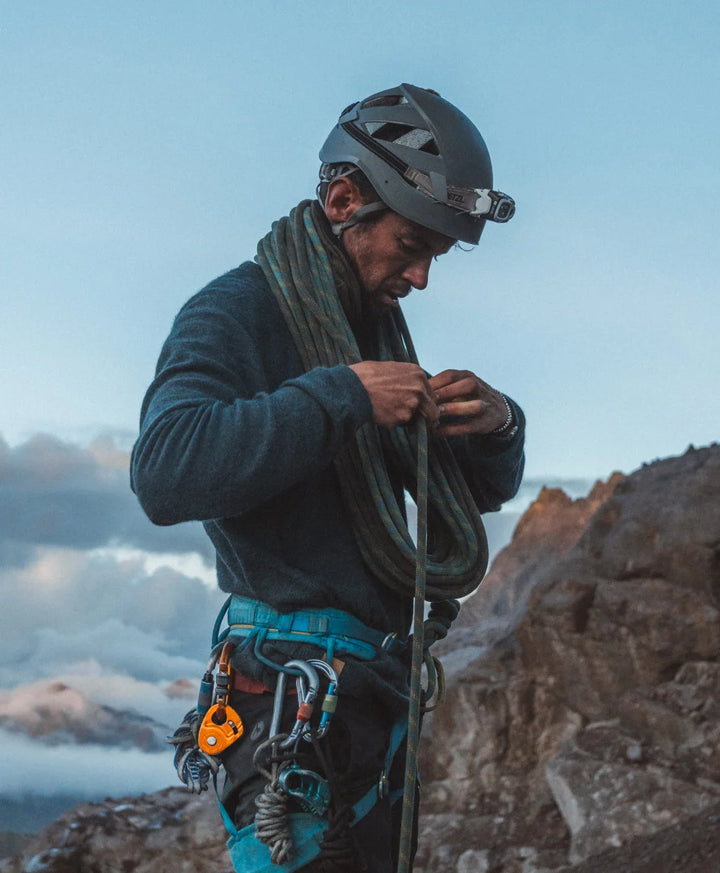 Climber adjusting gear on a rocky mountain slope under a cloudy sky