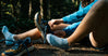 Two people sitting on rocks by a trail wearing socks and hiking shoes in an outdoor setting
