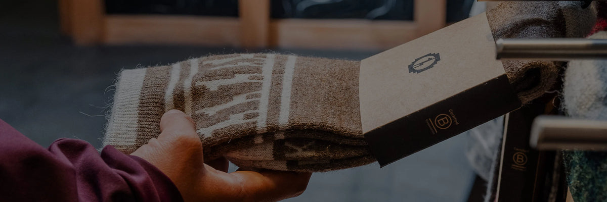 Person’s hand holding a folded brown patterned alpaca sock with a retail tag in a store setting