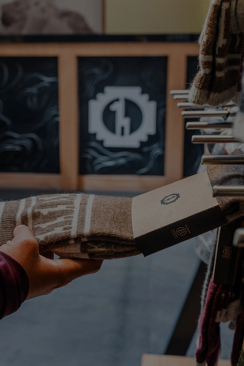 Customer hand pulling a packaged brown patterned sock from a store rack in a retail shop