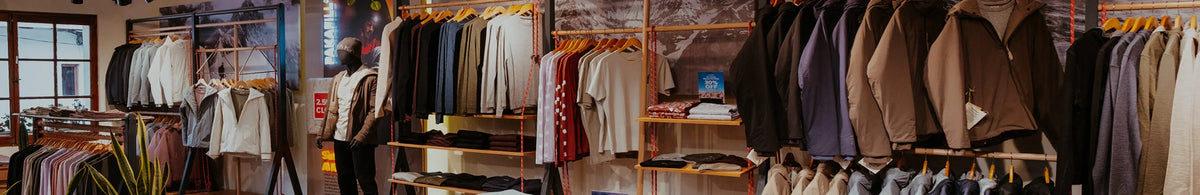 Mannequin modeling a jacket amid wooden racks of shirts and jackets in a warmly lit retail store