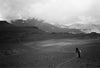 Single climber at a desolate high-altitude basecamp below rugged Chilean peaks under fast-moving clouds
