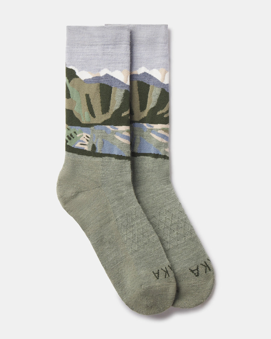 Flat lay of Essential Sacred Valley crew socks showing mountain landscape graphic in green, blue, and lavender on a light gray background