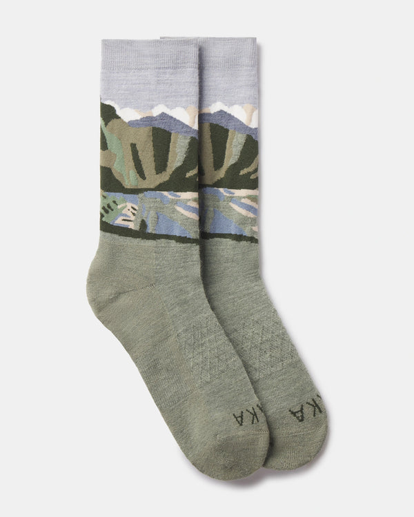 Flat lay of Essential Sacred Valley crew socks showing mountain landscape graphic in green, blue, and lavender on a light gray background