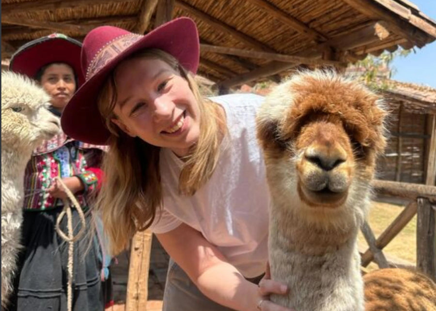 Woman with a pink hat interacting with an alpaca in a rustic setting
