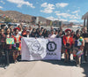 Seventeen Peruvian scholarship recipients standing outdoors holding a PAKA banner against a mountainous town backdrop