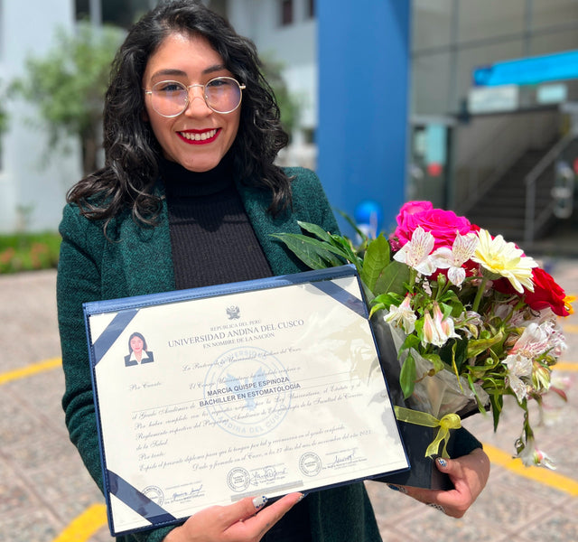 Young woman smiling and holding a framed diploma and bouquet outside a university building