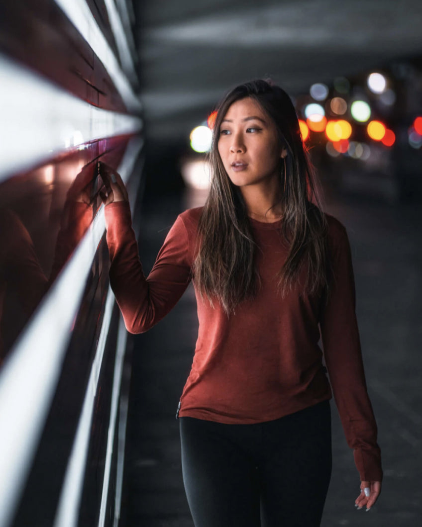 Woman Named Grace in Aire Clay / Red Alpaca and Tencel Long Sleeve Shirt Touching Illuminated Wall with City Lights in Background – PAKA Apparel