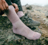 Side view of mauve performance crew sock on a hiker showing ribbed calf for grip and cushioned heel on rocky trail background
