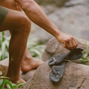 Hand placing charcoal grey socks on a rock outdoors