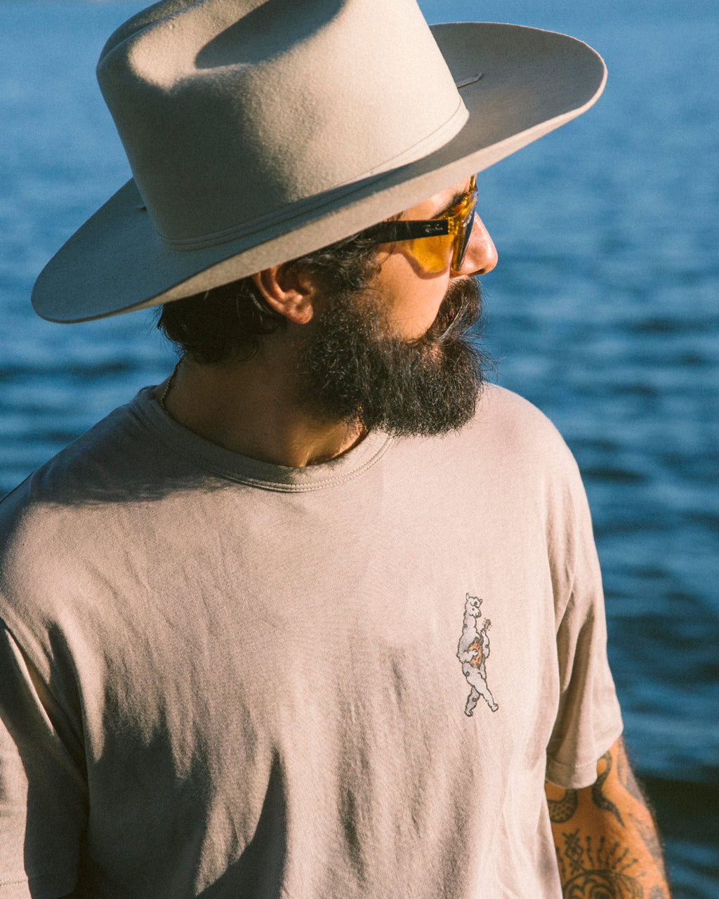 Person wearing a lightweight beige alpaca crewneck standing by the ocean on a sunny day