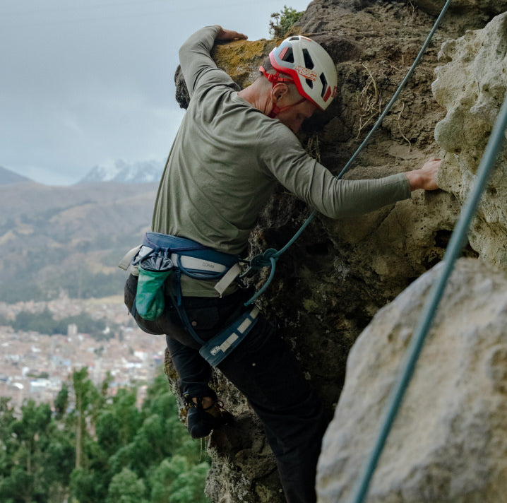 A man climbing rocks in his green Alpaca Baselayer