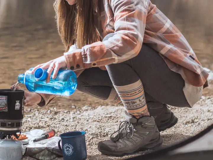 Woman boiling water outdoors by a river in her comfortable alpaca Inca socks