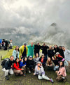 PAKA team posing together on a grassy overlook at Machu Picchu with misty mountains in the background