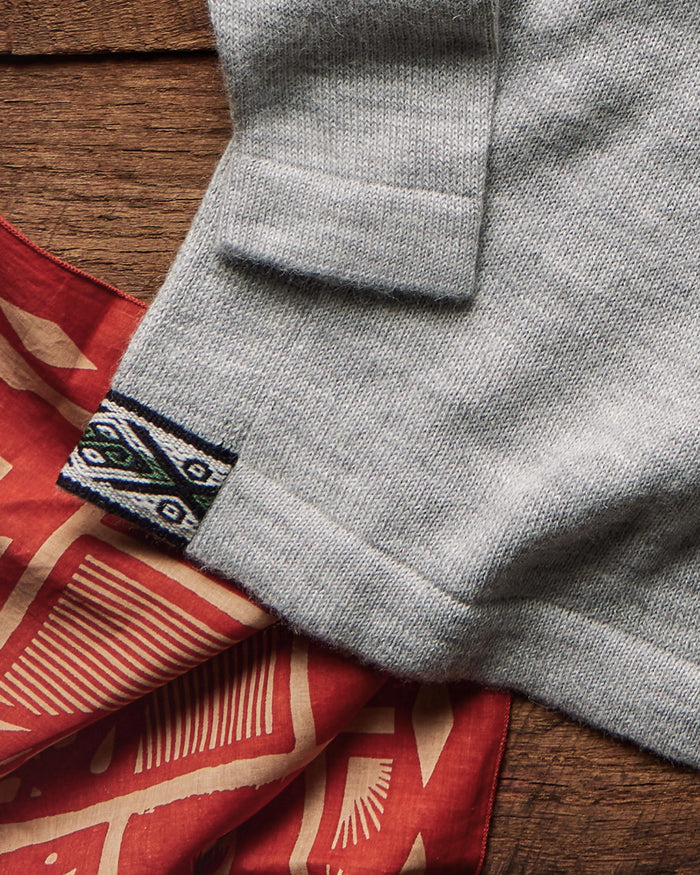 Close-up of The Original Crew alpaca crewneck showing light grey knit, folded cuff and woven hem tag on wood with red bandana