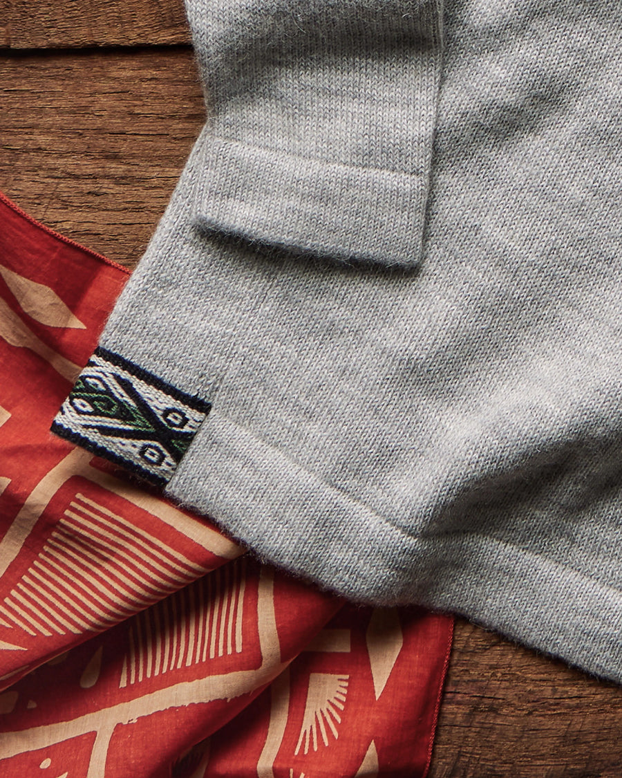 Close-up of The Original Crew alpaca crewneck showing light grey knit, folded cuff and woven hem tag on wood with red bandana