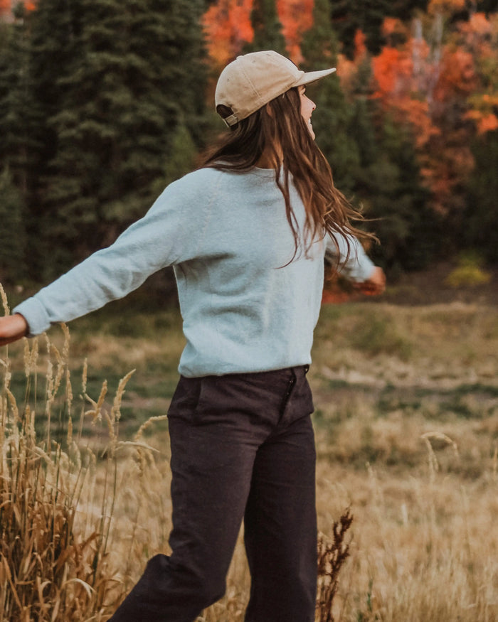 Woman spinning in a field wearing a sky blue alpaca crewneck sweater in a relaxed fit with autumn trees in the background