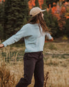 Woman spinning in a field wearing a sky blue alpaca crewneck sweater in a relaxed fit with autumn trees in the background