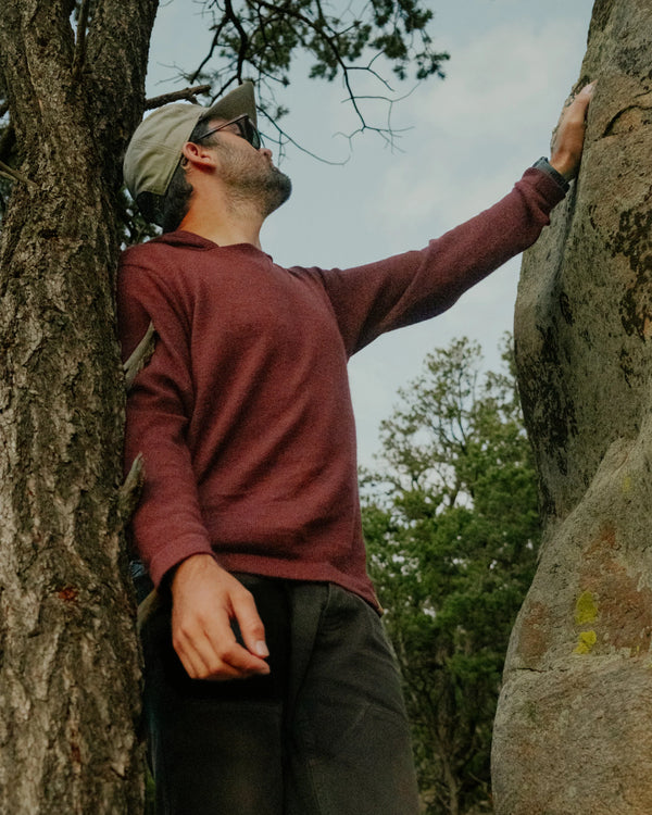 Low-angle view of burgundy alpaca hoodie on model showcasing textured knit, hood, and relaxed fit with trees and rocks background