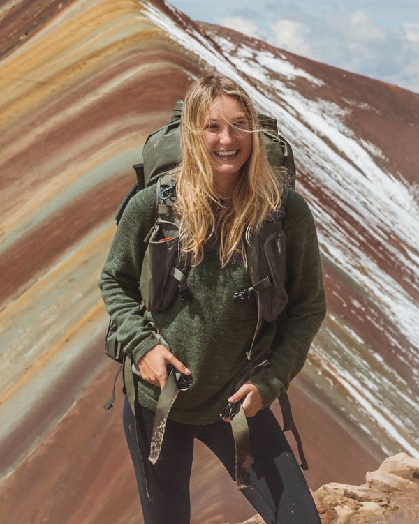 Woman hiking wearing eucalyptus green crewneck alpaca sweater, slim fit, with backpack in mountains