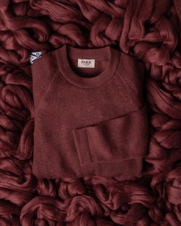 Top-down view of The Original Crew burgundy alpaca wool crewneck sweater showing crew neckline and ribbed hem on chunky yarn background