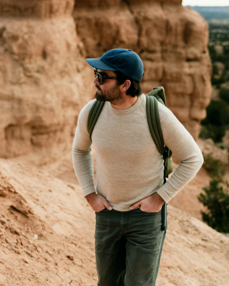 Man in Cap with Pack Hiking While Wearing The Original Crew Pebble / Beige Alpaca Sweater in Rocky Desert Landscape – PAKA Apparel
